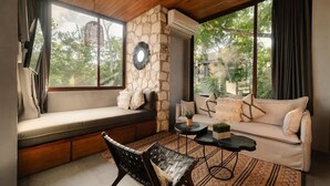 A cozy room with a stone wall, a sofa, a bench, and a table with a plant. - Siwa Jungle Solstice C1-102 (Tulum)