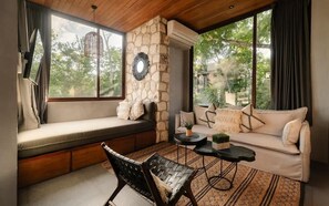 A cozy room with a stone wall, a sofa, a bench, and a table with a plant. - Siwa Jungle Solstice C1-102 (Tulum)