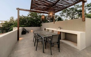 An outdoor patio with a table and chairs, a built-in bench, and hanging lights. - Siwa Jungle Solstice C1-102 (Tulum)