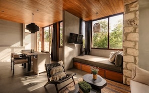 A modern living room with a sofa, a dining table, a TV mounted on the wall, and large windows. - Siwa Jungle Solstice C1-102 (Tulum)