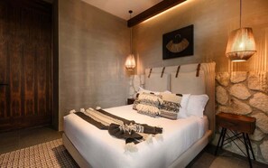 A bedroom with a large bed, a wooden door, a stone wall, and a hanging light fixture. - Siwa Jungle Solstice C1-102 (Tulum)