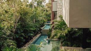 A pool surrounded by lush greenery and a stone wall. - Siwa Jungle Solstice C1-102 (Tulum)