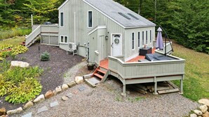 A two-story cabin with a deck, surrounded by a garden and forest. - Home at Waterville Estates- tons of amenities! (Campton)