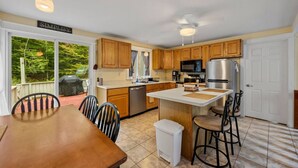A kitchen with wooden cabinets, a stainless steel refrigerator, a microwave, and a dining area with a table and chairs. - Home at Waterville Estates- tons of amenities! (Campton)