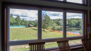 A room with large windows overlooking a grassy area, a small structure, and a body of water. - Home at Waterville Estates- tons of amenities! (Campton)