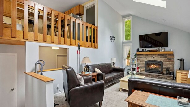 A spacious living room with a fireplace, leather sofas, a wooden staircase, and a television mounted on the wall. - Home at Waterville Estates- tons of amenities! (Campton)