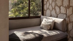 A cozy room with a stone wall, a window with a woven light fixture, and a cushioned bench with pillows.