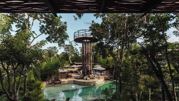 A water park with a central pool, a lookout tower, and surrounding lush greenery.