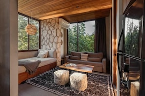 Ein modernes Interieur mit einer Steinwand, einem Sofa, einem Couchtisch und einem großen Fenster mit Blick auf Grünflächen.