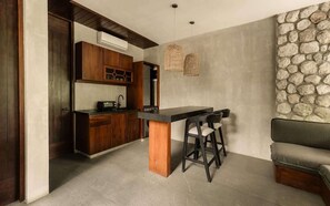 A modern kitchen with wooden cabinets, a central island, bar stools, and a stone accent wall. - Siwa Jungle Rain A2-004 Beach Club Access (Tulum)