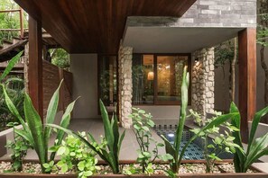 A modern building with a stone facade, a wooden ceiling, and a glass door leading to a room. - Siwa Jungle Rain A2-004 Beach Club Access (Tulum)