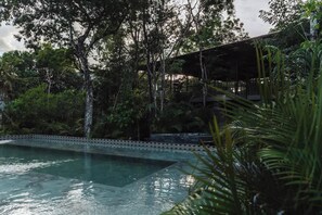 En pool omgiven av frodig grönska och en överbyggd konstruktion.