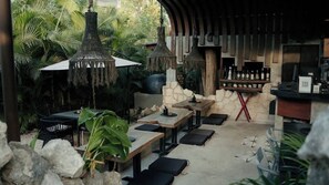 Een terras met tafels en stoelen, omgeven door tropische planten en een stenen muur.