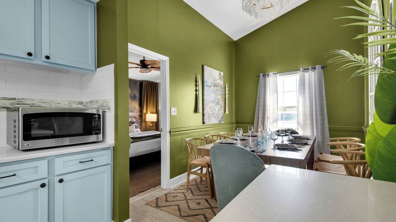 A kitchen with a microwave, light blue cabinets, and a dining area with a table set for two.