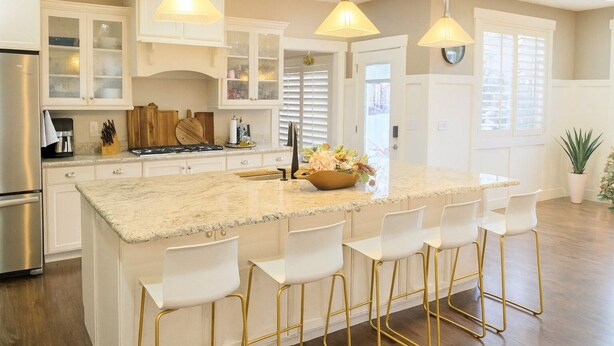 Een moderne keuken met een groot eiland, witte barstoelen en hanglampen.