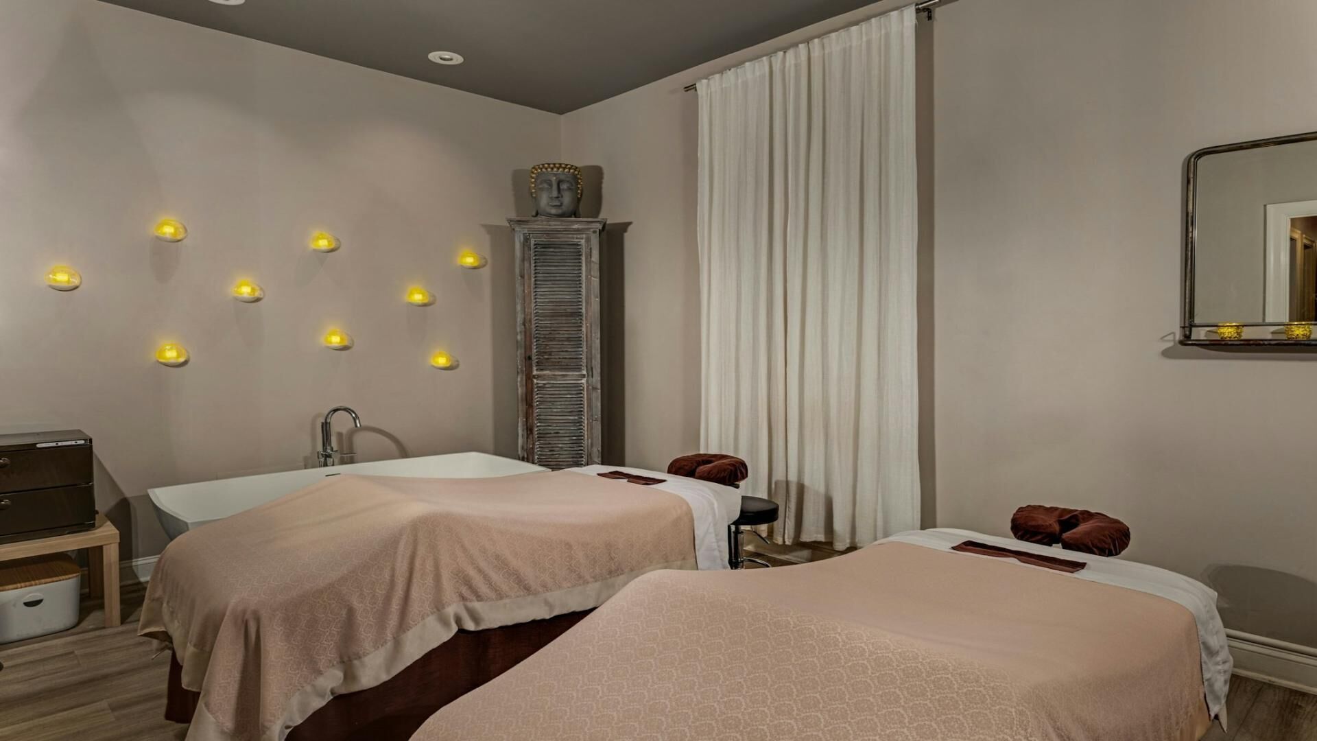 Une chambre d’hôtel avec deux lits, une coiffeuse, un miroir et des lampes fixées au mur.