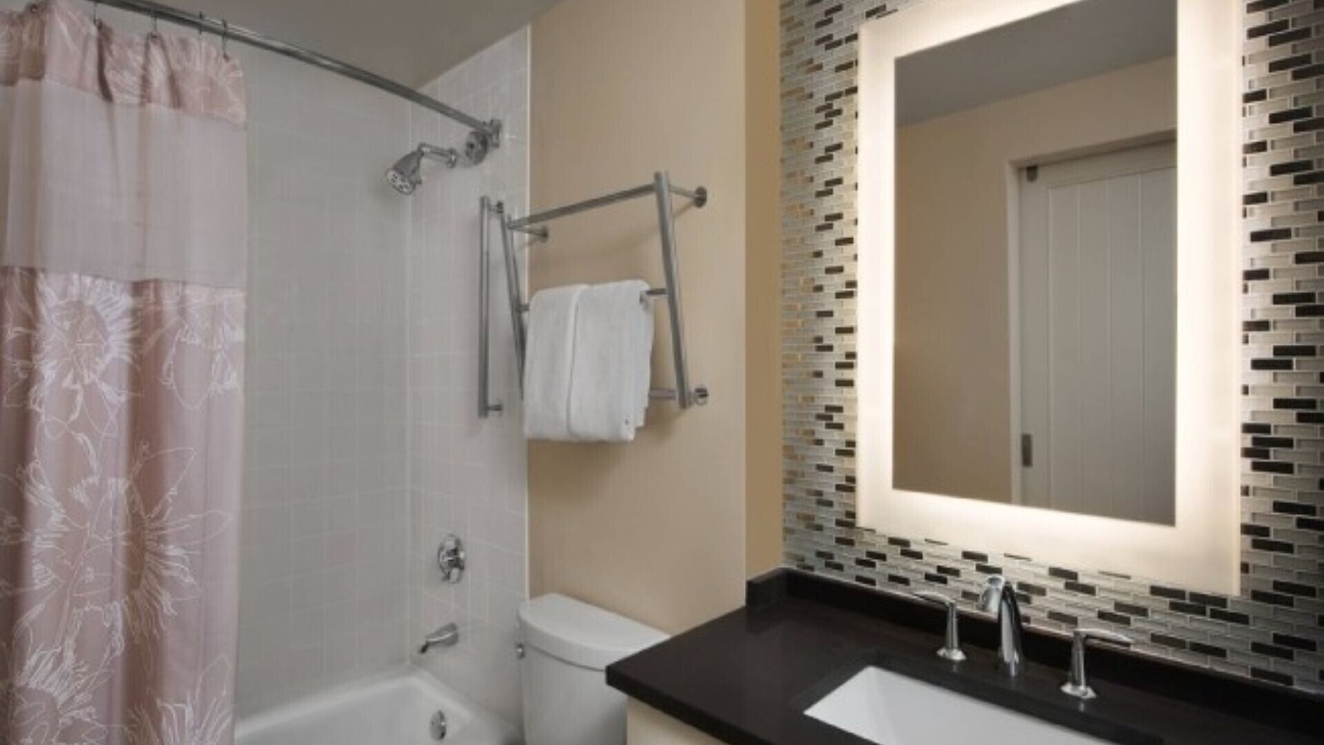 Et badeværelse med brusebad, toilet, vask og et spejl med mosaik bagvæg.