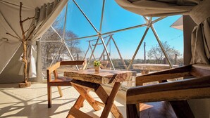 Una carpa con una mesa de madera y sillas, una planta en maceta y una vista despejada al exterior.
