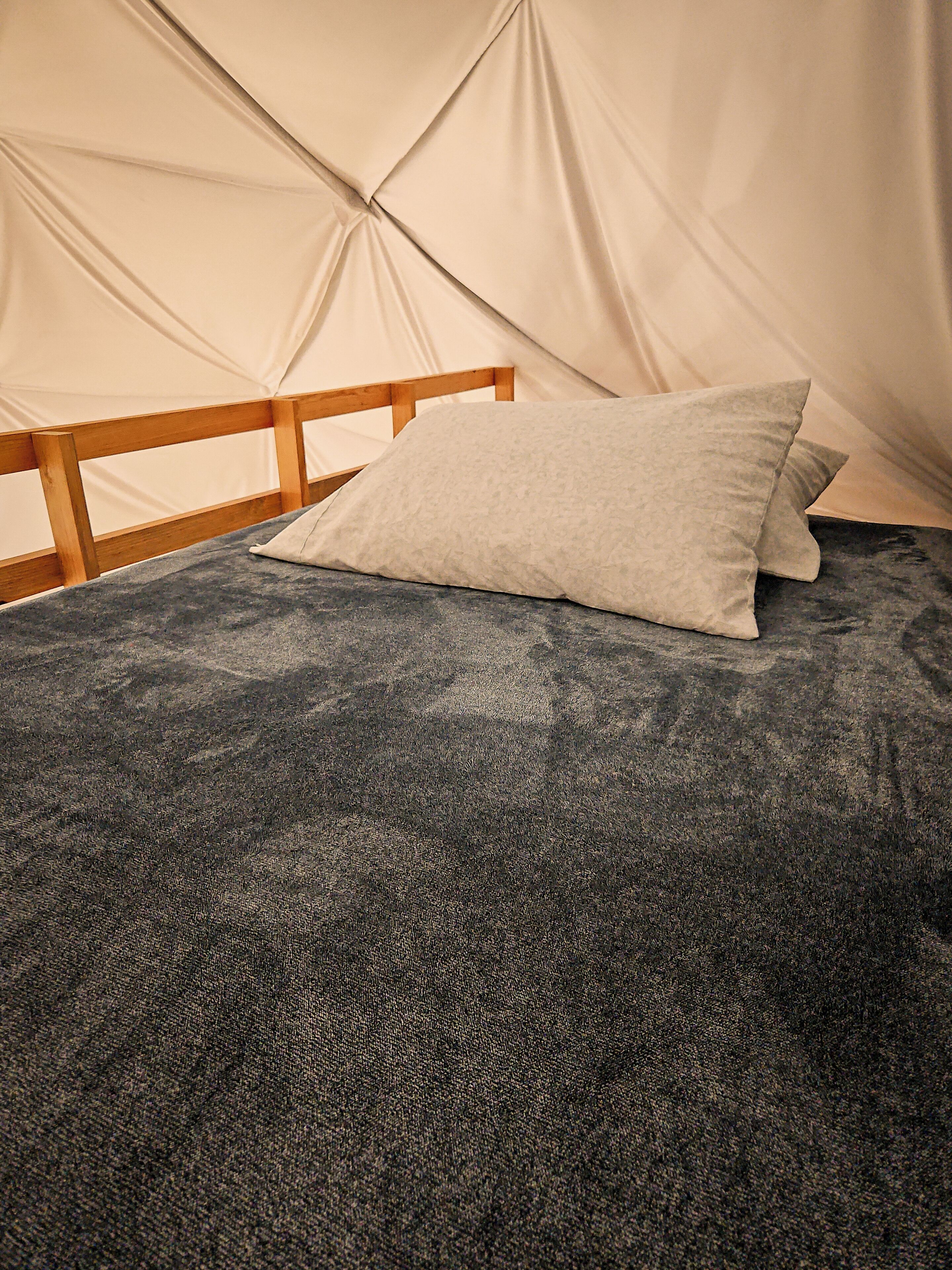 A tent with a wooden headboard and a grey textured bedspread.