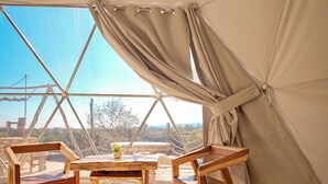 Una carpa con una mesa, sillas y un cojín verde, con vistas al exterior.