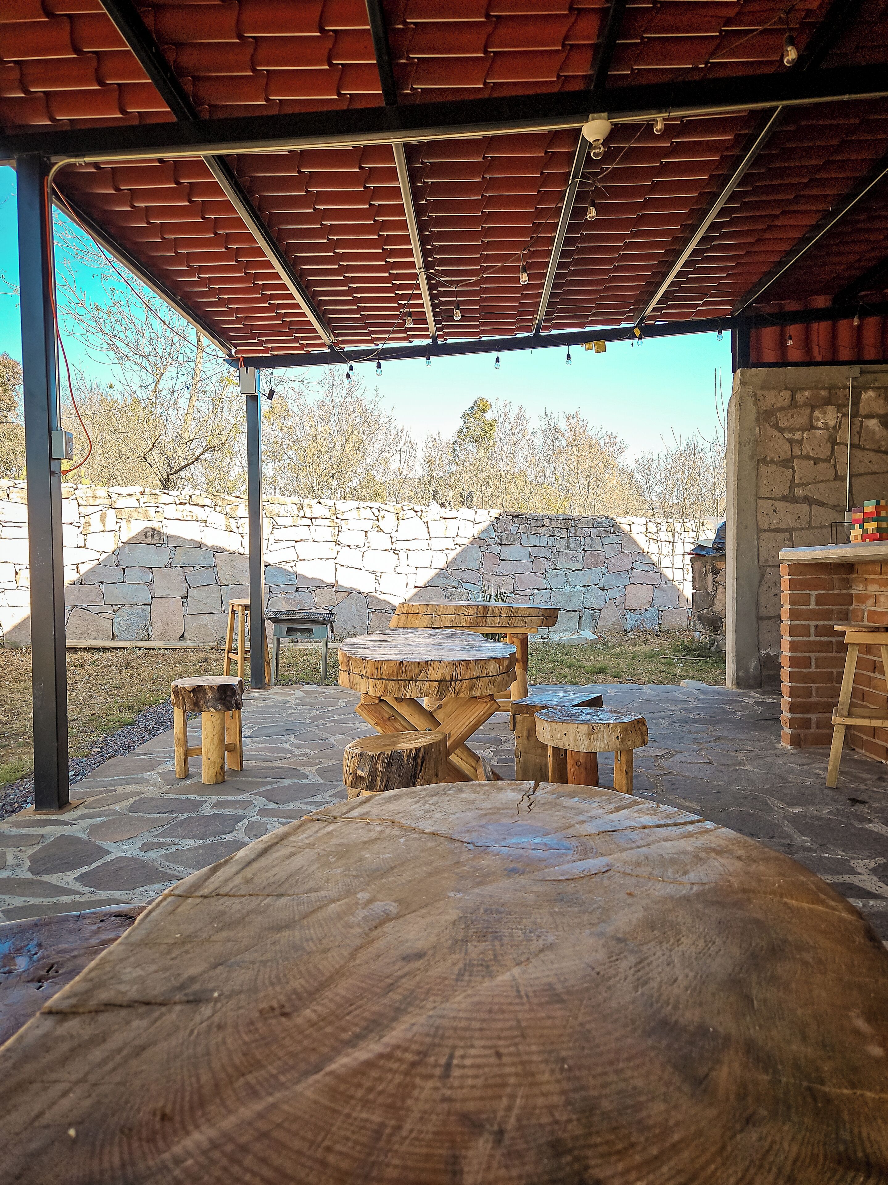 An outdoor patio area with stone walls, a wooden table, and benches.