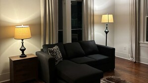 Ein modernes Wohnzimmer mit einem schwarzen Sofa, zwei Lampen, einem Holznachttisch und einem gemusterten Teppich.