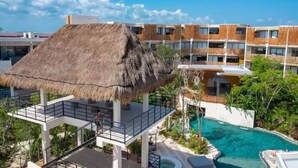 A hotel with a thatched-roof structure, a swimming pool, and a multi-story building in the background. - Near Tulum Beach 2BR –Private Pool & Cenote Access (Tulum)