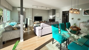 Ein modernes Wohnzimmer mit einem Glastisch, blaugrünen Stühlen und einem grauen Sofa.