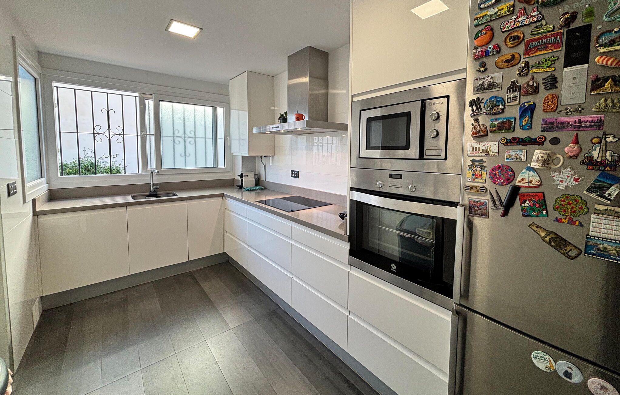A modern kitchen with white cabinets, a stainless steel refrigerator, and a window with bars.