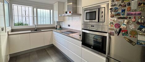 A modern kitchen with white cabinets, a stainless steel refrigerator, and a window with bars.