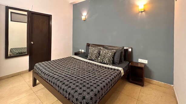 A bedroom with a bed, nightstands, a mirror, and two wall-mounted lights. - Skyline Stay (Gurugram)
