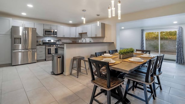 Cozinha moderna com eletrodomésticos de aço inoxidável, sala de jantar com mesa e cadeiras de madeira, e uma janela grande com cortinas.