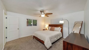 Quarto com cama, ventilador de teto, abajur, janela e espelho.