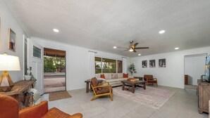Uma sala de estar ampla, com sofá, cadeiras, mesa de centro e ventilador de teto.