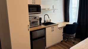 Eine kompakte Küchenzeile mit Mikrowelle, Toaster und Kaffeemaschine, einem kleinen Spülbecken und einem Stuhl.