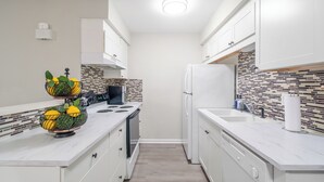 A modern kitchen with white cabinets, a tiled backsplash, and a central island with a fruit bowl. - Ballantyne Retreat – Updated 2BR/2BA Near Shops & Medical (Charlotte)