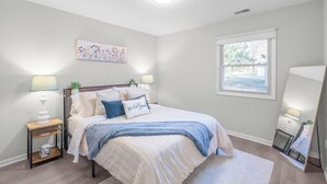 A bedroom with a bed, bedside tables, a nightstand, a mirror, a window, and a wall-mounted artwork. - Ballantyne Retreat – Updated 2BR/2BA Near Shops & Medical (Charlotte)