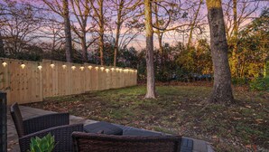 An outdoor patio area with wicker furniture, a wooden fence, and trees. - Ballantyne Retreat – Updated 2BR/2BA Near Shops & Medical (Charlotte)