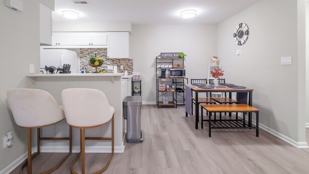 A modern kitchen with white cabinets, a built-in microwave, and a coffee bar. There are two bar stools and a dining table with chairs. - Ballantyne Retreat – Updated 2BR/2BA Near Shops & Medical (Charlotte)
