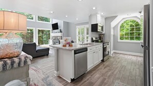 Una cocina moderna con una isla central, armarios blancos y ventanas amplias.
