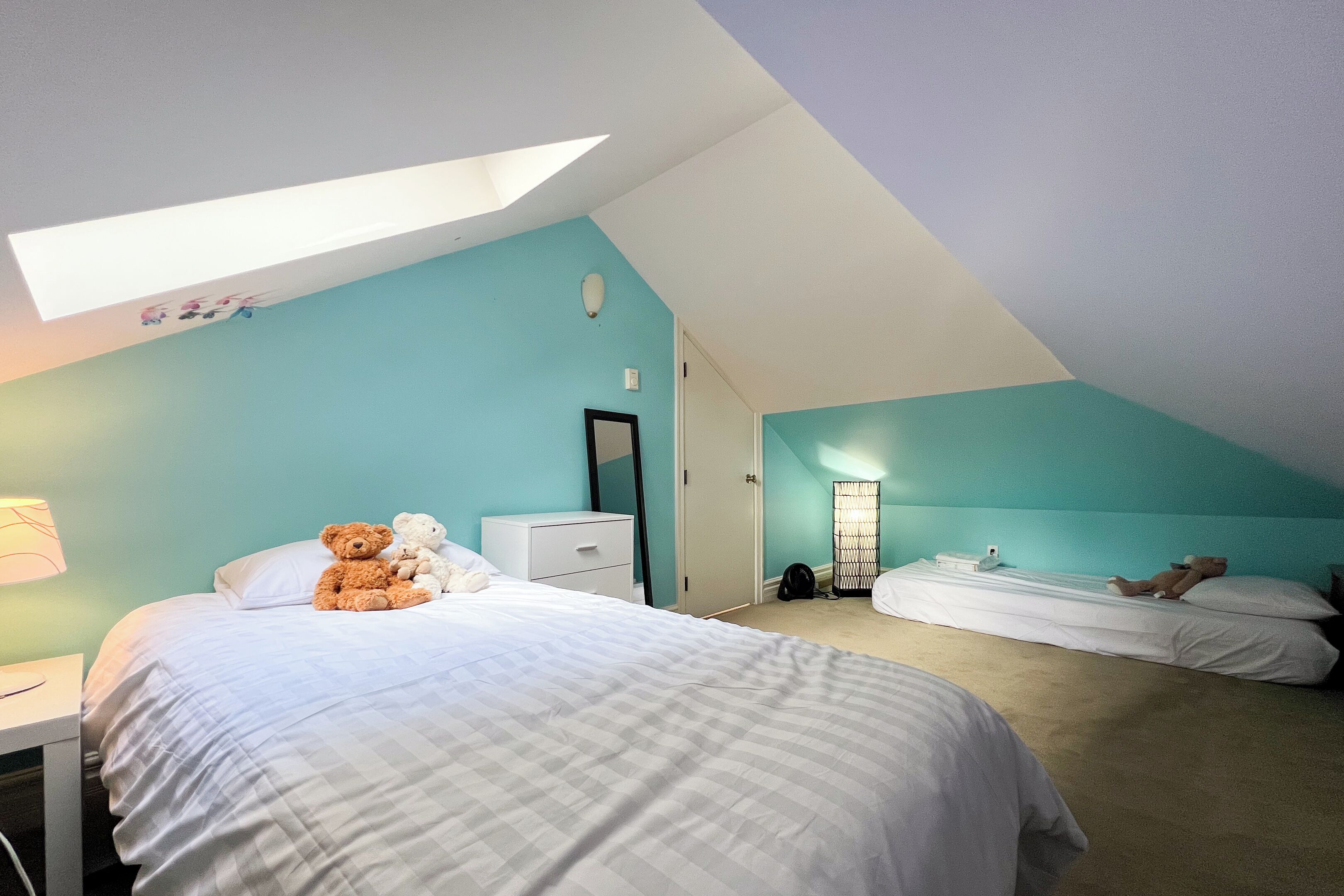 A bedroom with a skylight, two beds, a dresser, and a bedside lamp.