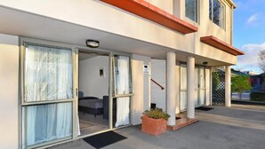 Ingresso di un hotel con porta in vetro, una piccola area salotto esterna e una pianta in vaso.