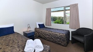 Una camera d'albergo con un letto, una panca, una sedia, un comodino e una finestra con tende.
