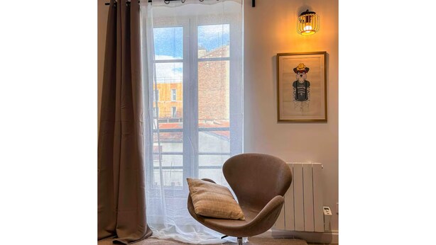 Et moderne værelse med et stort vindue, en stol med pude, en radiator og et billede i ramme på væggen.