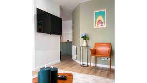En moderne stue med et fladskærms-tv på væggen, et træ sofabord, en teal vase med blomster og en brun læderstol.