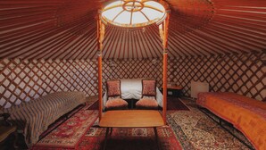 Een traditioneel ingerichte joert met een centraal bed, twee kleinere bedden en een houten tafel.