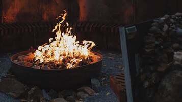 A fire pit with flames, surrounded by rocks and gravel, in an outdoor setting with a building in the background.