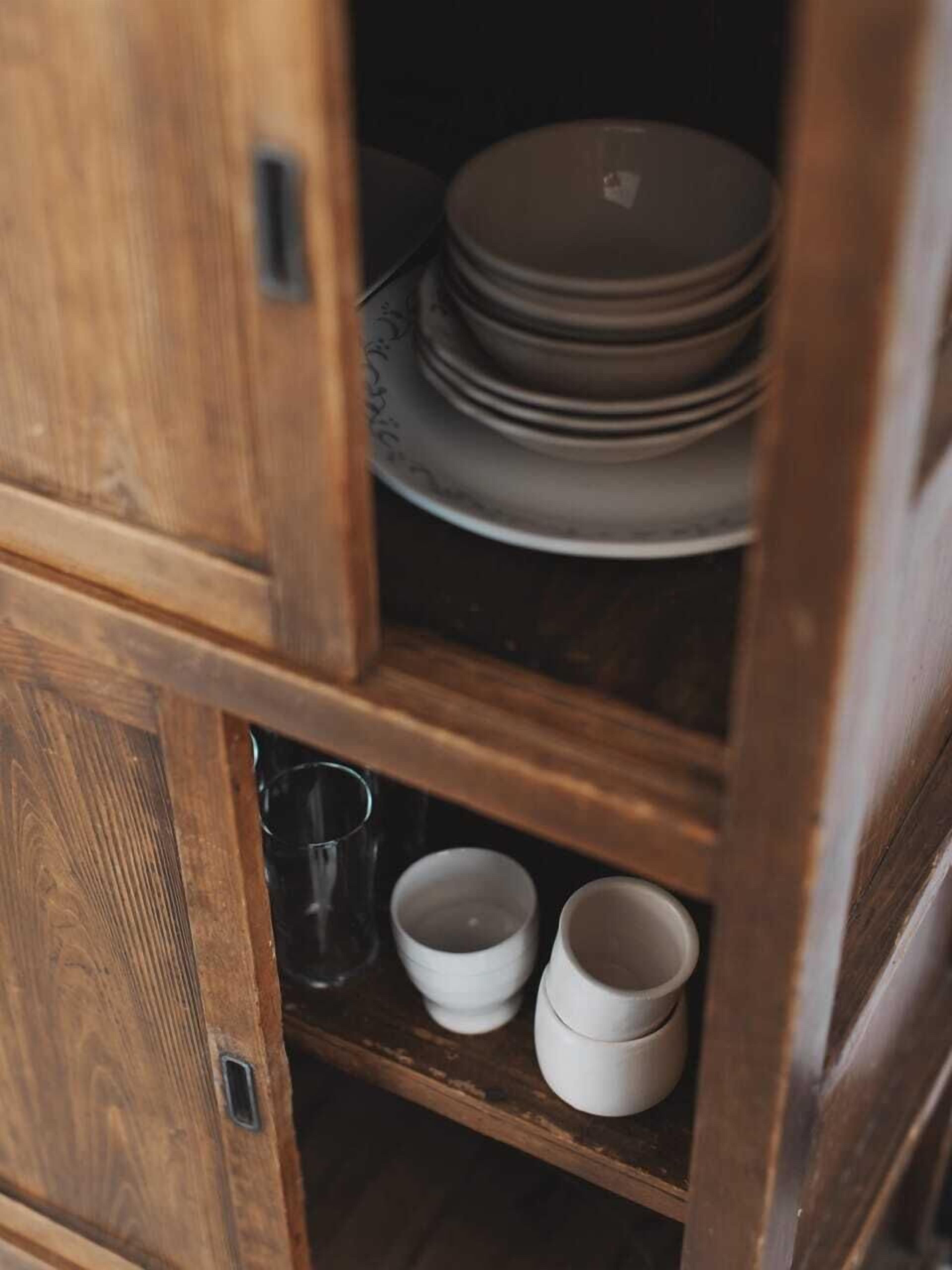 A wooden cabinet with shelves containing stacked plates, bowls, and a glass.