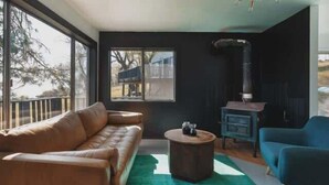 Ein modernes Wohnzimmer mit einem Ledersofa, einem runden Couchtisch und einem blauen Sessel. Ein großes Fenster bietet einen Blick ins Freie.