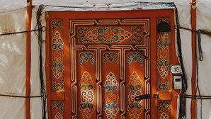 Une yourte traditionnelle, dotée d’une porte en bois décorative, d’une plaque d’immatriculation et d’une corde enroulée autour de l’entrée.